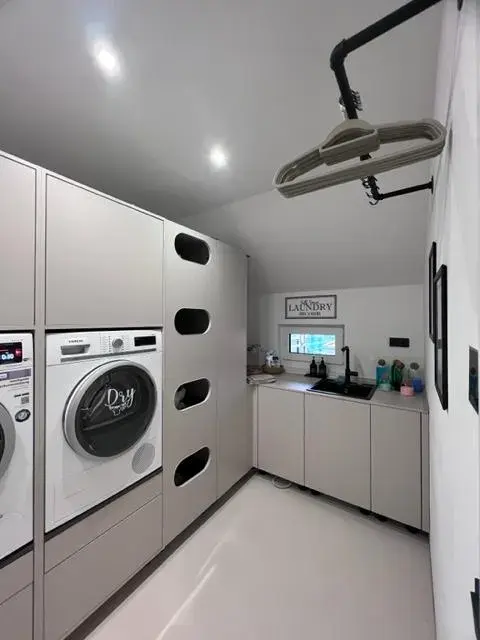 Moderner, weißer Hauswirtschaftsraum mit Waschmaschine, Trockner und Wäschekorb-Öffnungen.