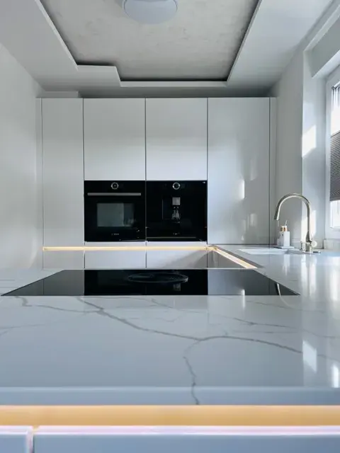 Moderne, weiße Küche mit Marmorarbeitsplatte und eingebauten Elektrogeräten.