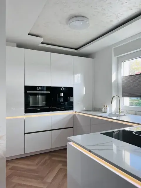 Moderne weiße Küche mit glänzenden Fronten, Einbauofen und Kochinsel.