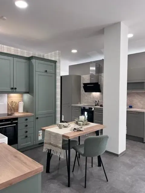 Moderne Küche mit grünen Schränken, Holztisch und zwei Stühlen.