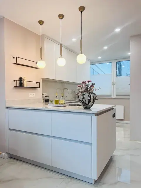Moderne Küche mit weißer Insel, drei Hängelampen und Vase mit Blumen
