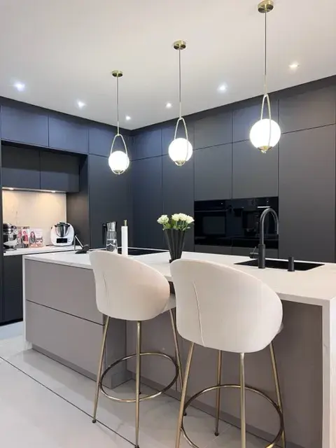 Moderne Küche mit grauen Schränken, Kücheninsel und zwei weißen Barhockern.