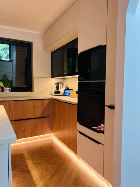 Moderne Küche mit Holzfronten, Unterbau-Beleuchtung und schwarzen Elektrogeräten.