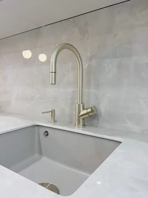 Moderne Spüle mit silbernem Wasserhahn vor hellgrauer Marmorwand
