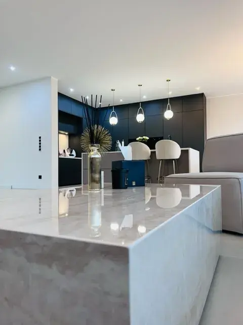Modernes Wohnzimmer mit Marmor-Tisch, offener Küche und Hängelampen.