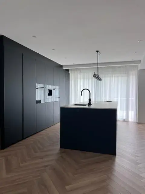 Moderne, minimalistische Küche mit dunkler Kücheninsel und Hängelampe.