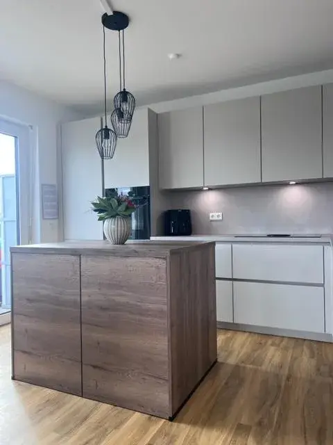 Moderne Küche mit Holzinsel, weißen Schränken und Hängelampen, helle Atmosphäre.